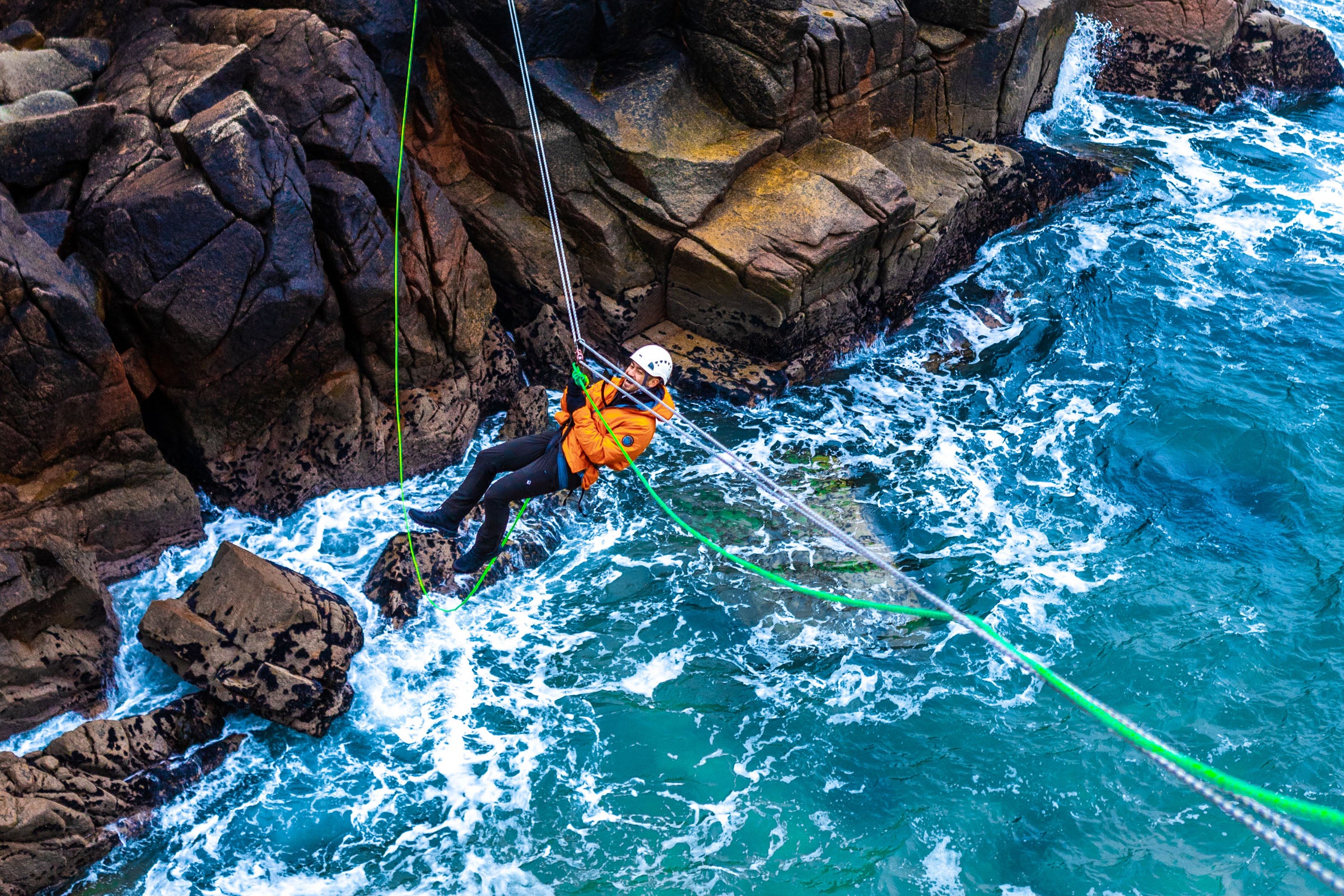 Climber crossing a Tyrolean Traverse rigged above the sea, Cruit Island, County Donegal