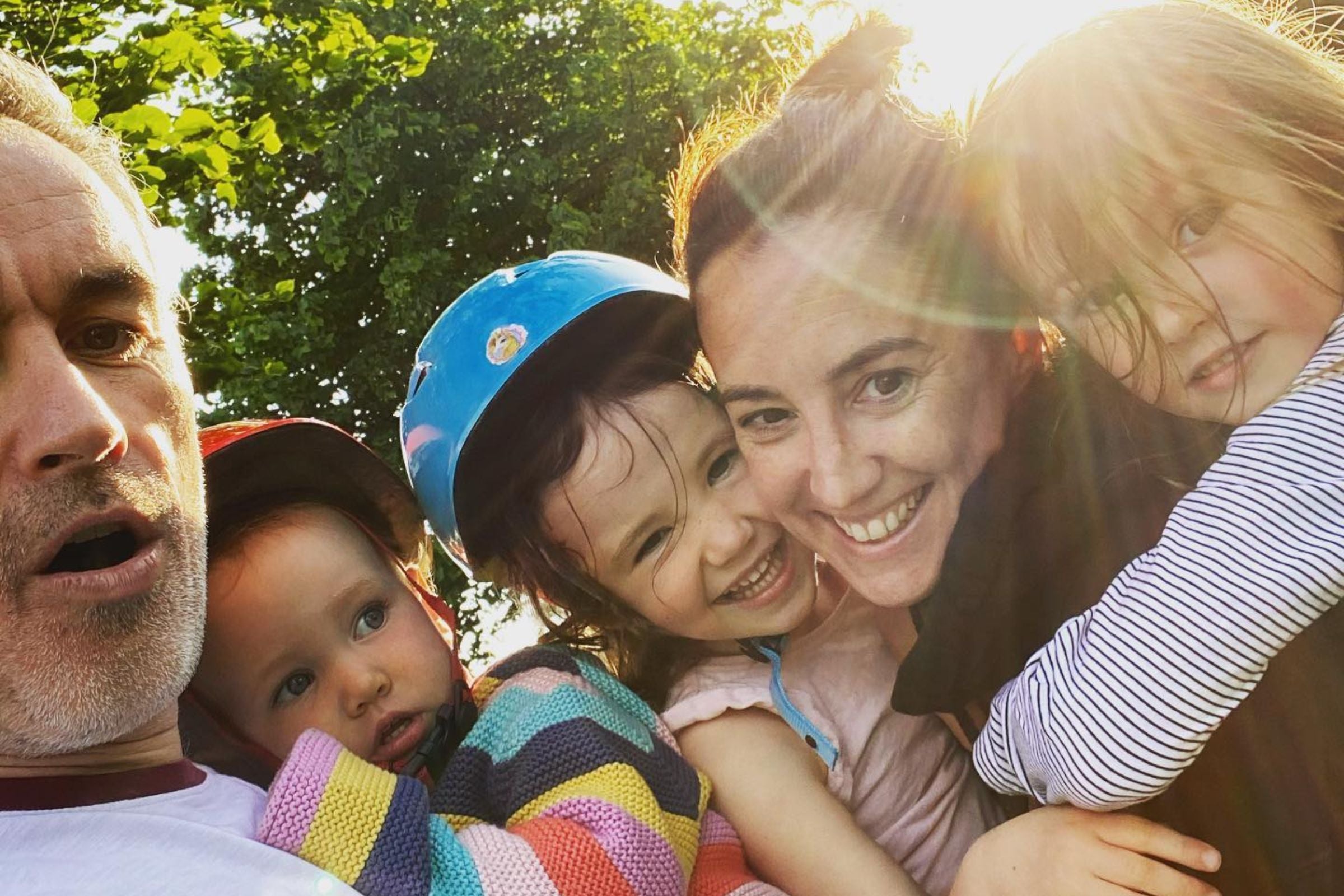 A family smiling at the camera with the sun shining behind them.