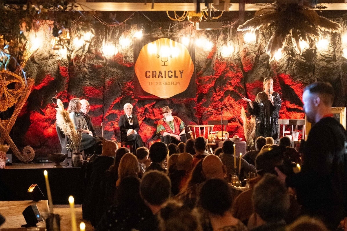 Puca Festival: Craicly Stories, a room with people seated at long dinner tables, looking towards people seated on small stage