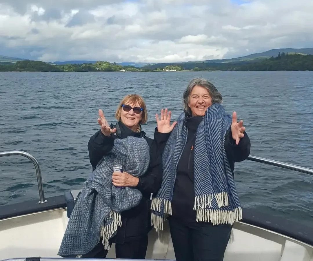 Two people smiling on a boat with the sea and mountains in the background