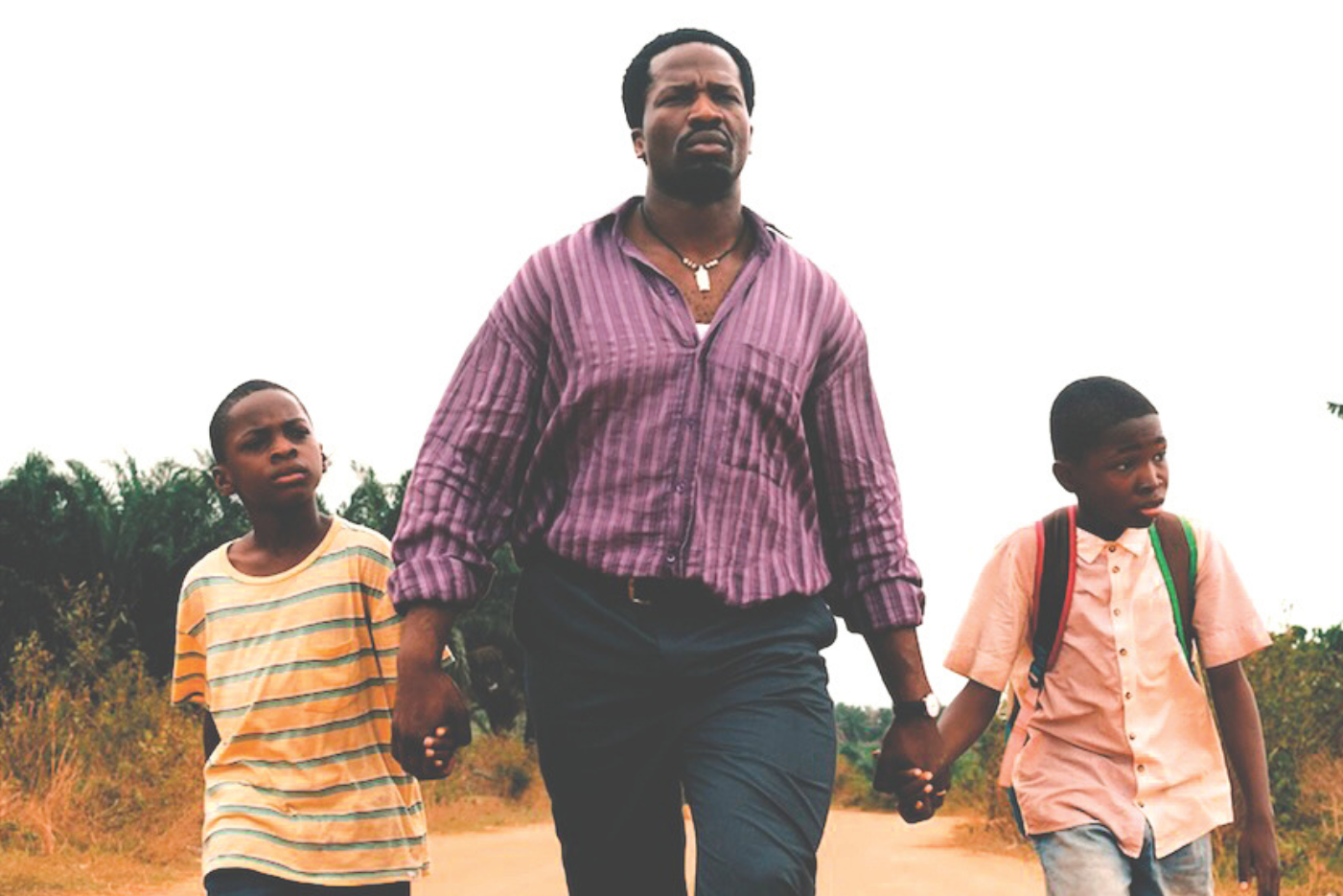 A determined looking man is walking along a road holding the hand of 2 young boys either side of him.