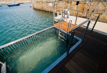 Enclosed sea plunge pool with steps and railing set on a harbour dock beside stone walls