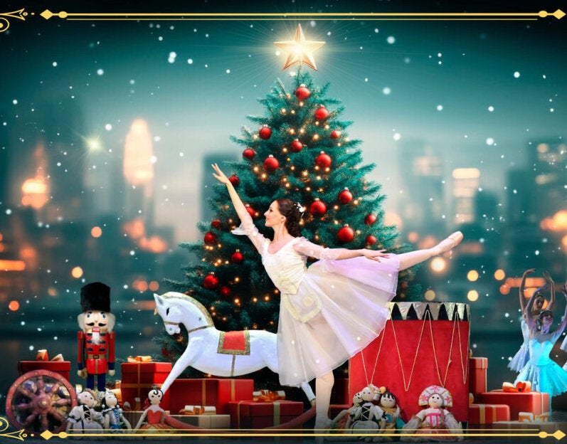 A woman in white dress is standing on one leg in ballet pose with other leg and arm outstretched, with christmas tree and toys behind.
