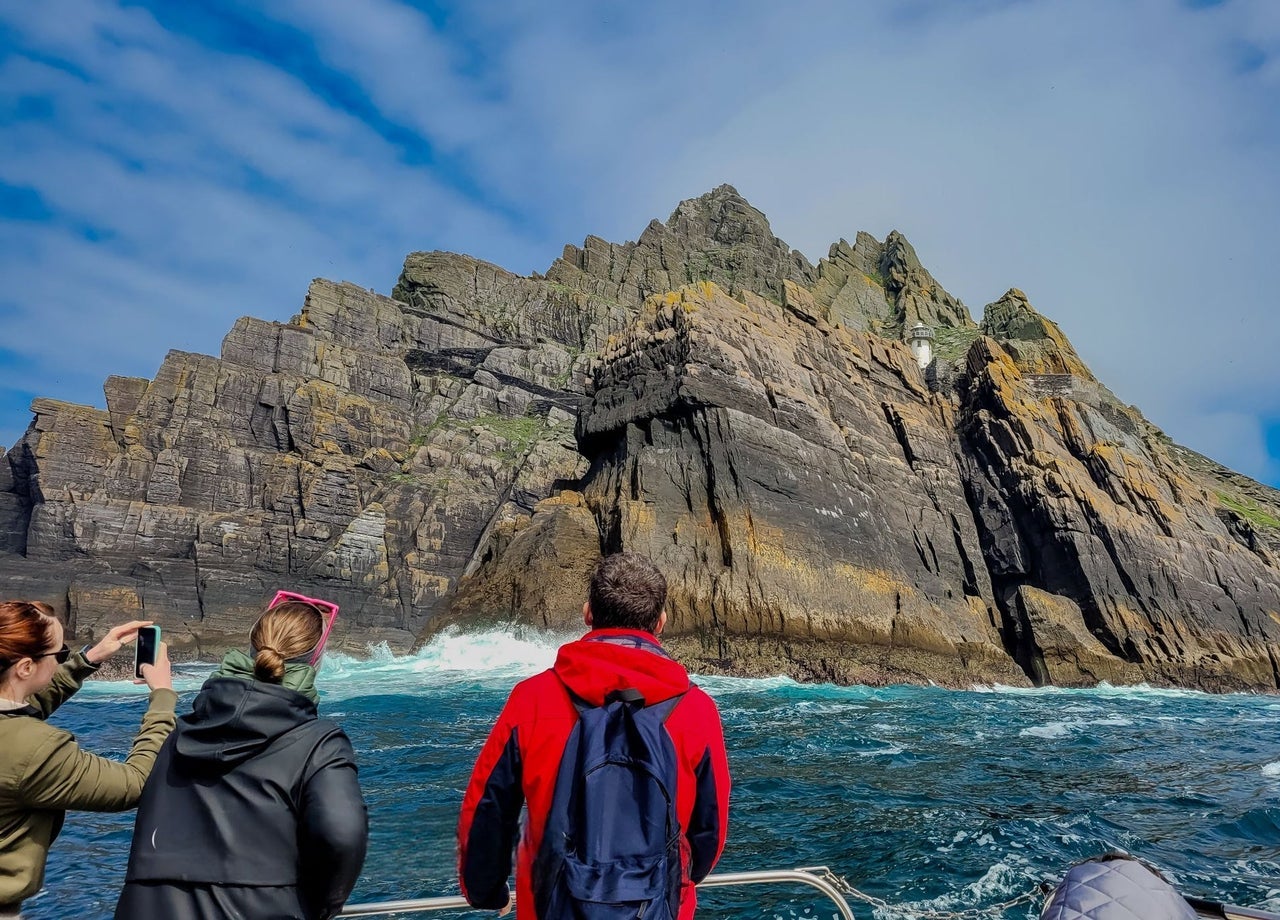 Three passengers on a tour boat taking photos of Small Skellig island