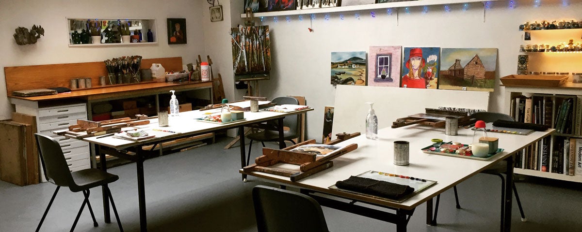 A view of the interior of the studio classroom with various painting materials on the tables and paintings on display on the walls
