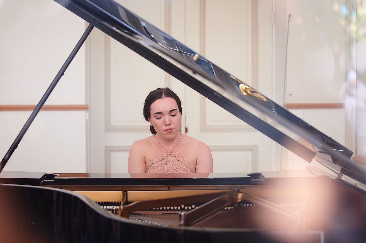 Looking through the open lid of grand piano at a woman playing at the keyboard.