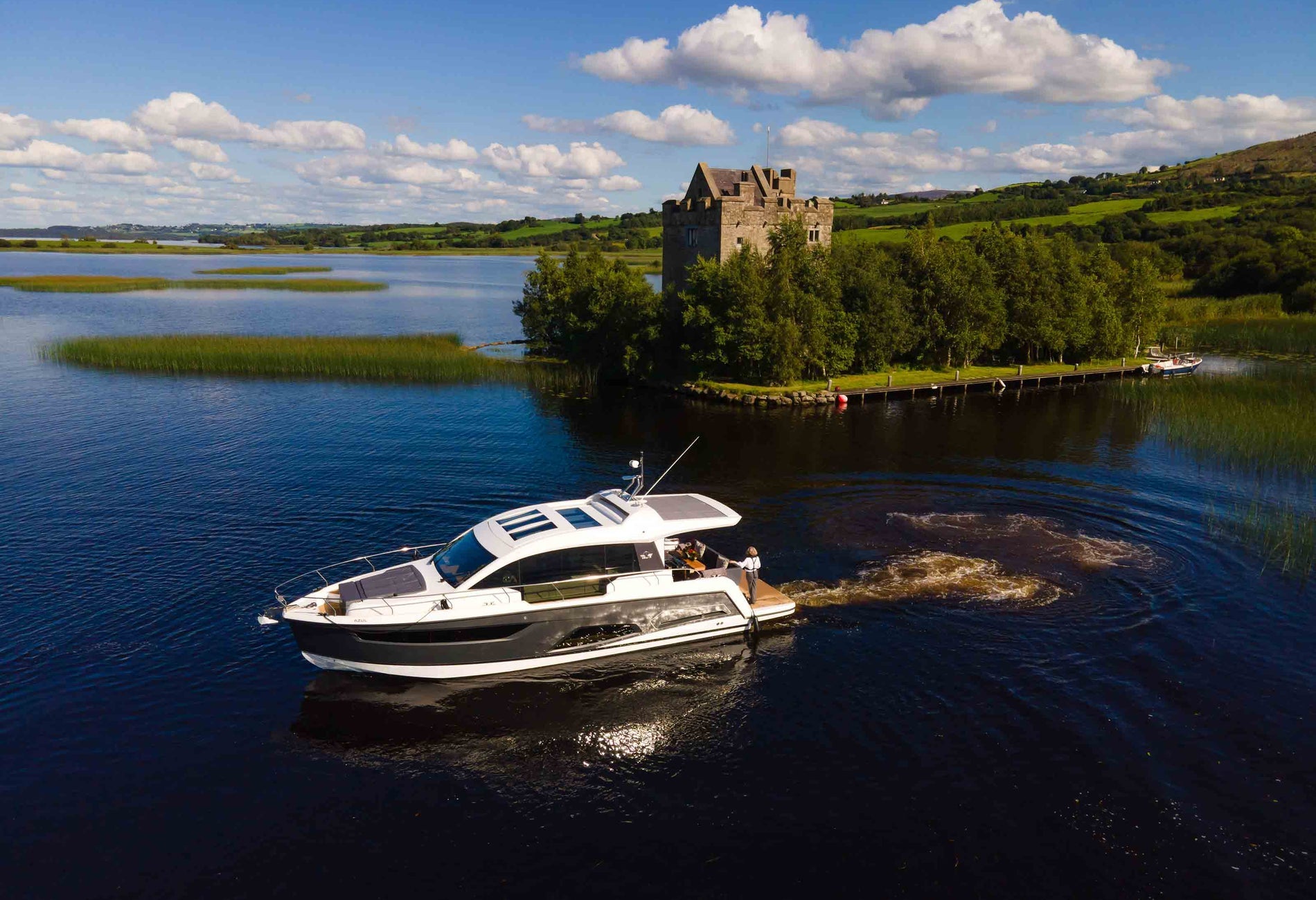 A boat on a large lake beside a small island with a castle surrounded by trees