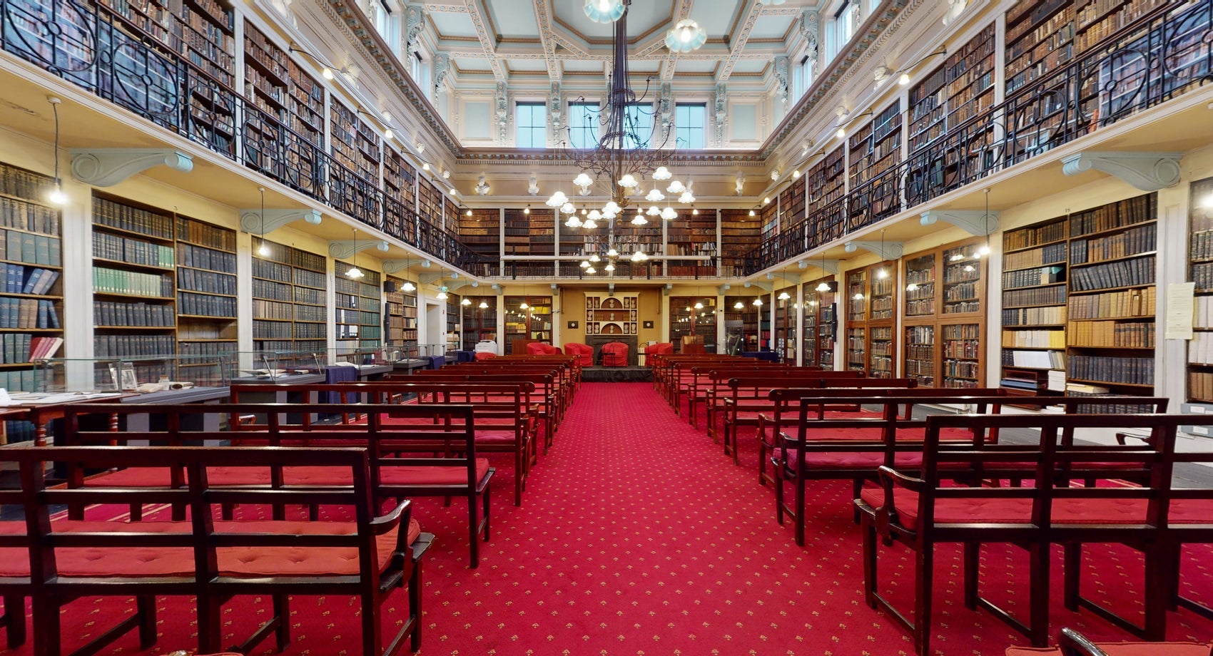 A library with wall to wall books and shelves with tables and chairs in a row
