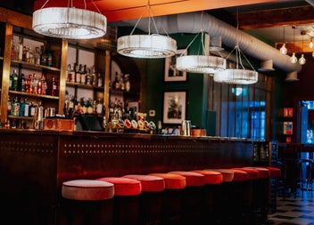 A bar counter with red covered stools and hanging lights