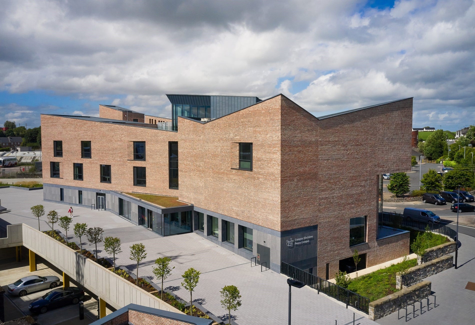 Grey and light brown building with trees by a path and cars parked outside
