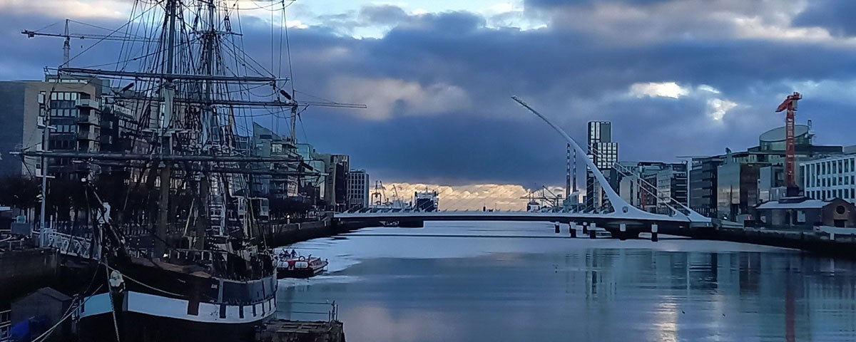 View of an old sailing ship with a bridge in background at sunset