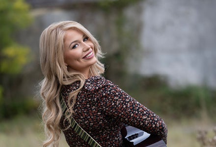 A smiling woman playing a guitar looking back over her right shoulder