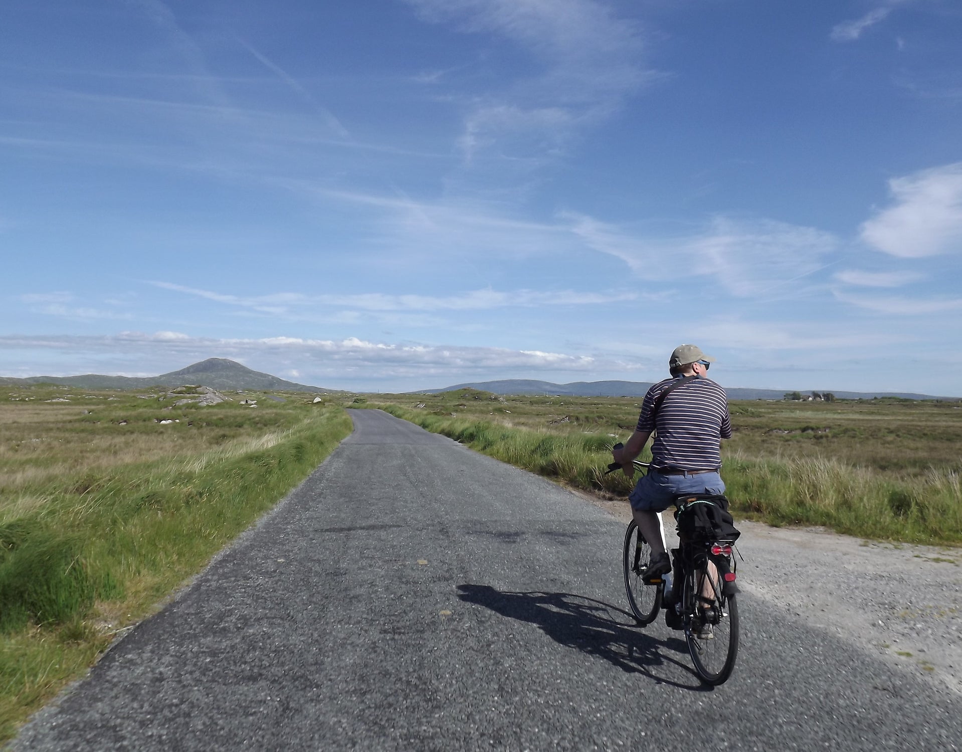 Person cycling on a road with fields either side and mountains in the background