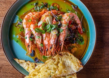 A plate of prawns in oil with fresh herbs alongside slices of toasted bread