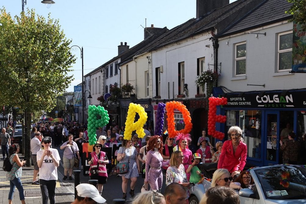 A parade is making it's way along a main street in a town with large different coloured letters made out of balloons.