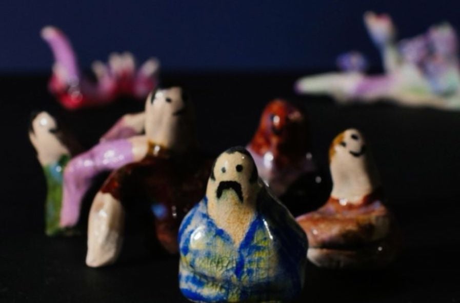 Out of focus image of small, roughly made painted ceramic figures against black background.