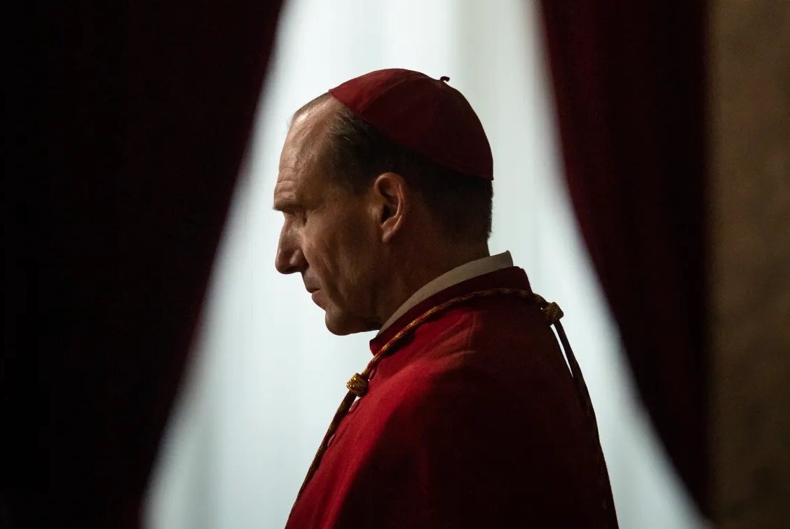 Side profile of a man in red church robes with small cap .