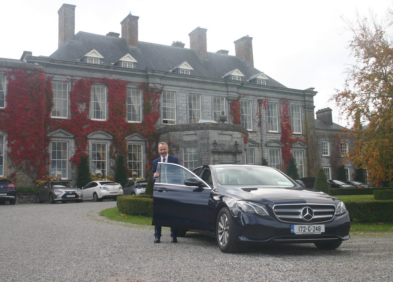 Man standing at car with ivy clad house in background