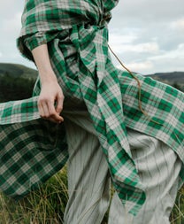 A close up of a lady wearing a large green tartan wrap around type of clothing standing on grass outdoors