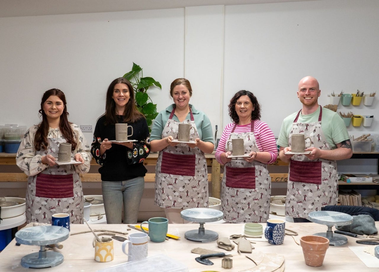 Five people with their pottery pieces standing at a table with aprons on them