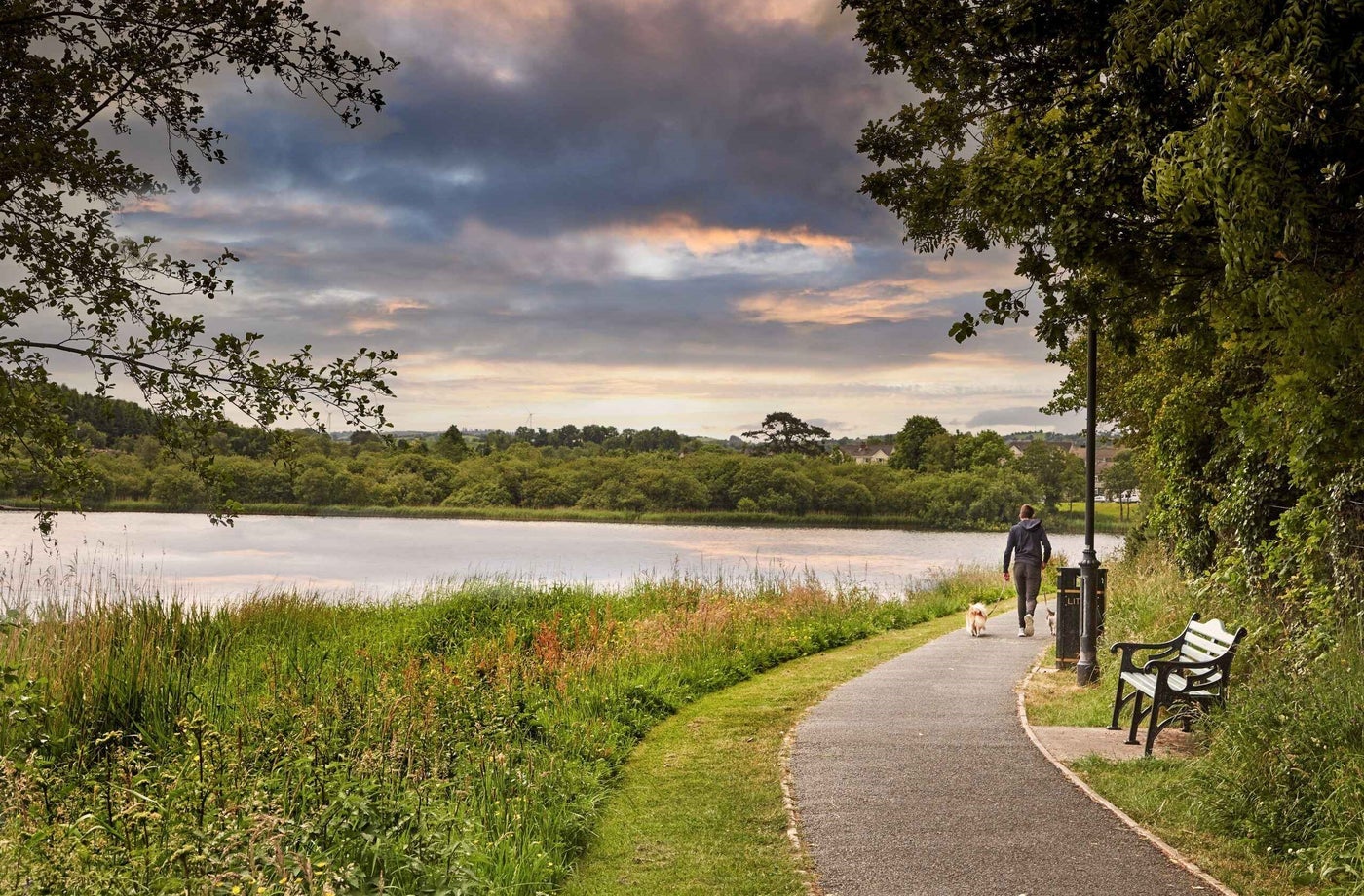 A person walking a dog along a lake side pathway