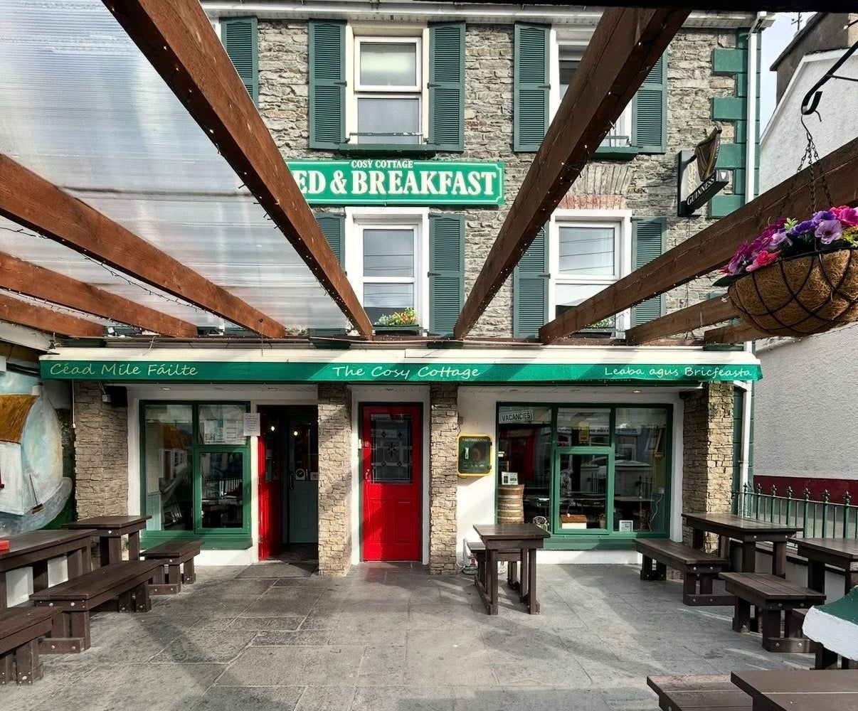 Exteriors of a coffee shop with a red door and green awning and benches in a courtyard