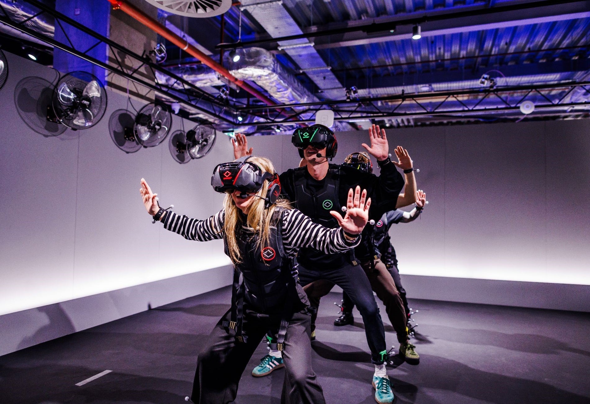 Four people wearing virtual reality headsets sanding in a line with their hands in the air