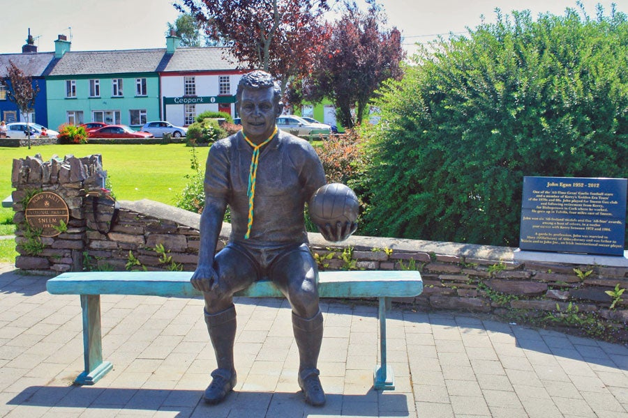 Bronze statue of footballer John Egan in seated pose with a football in hand
