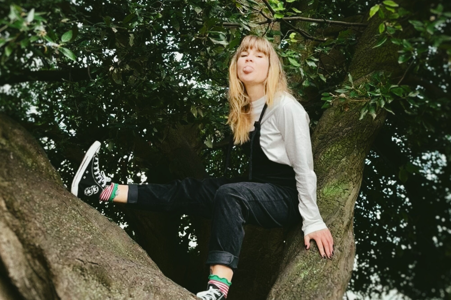 A woman is seating up a tree poking her tongue out.