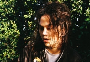 underground phenom Feng, a man with face partially obscured by hair, outside in dappled shade.