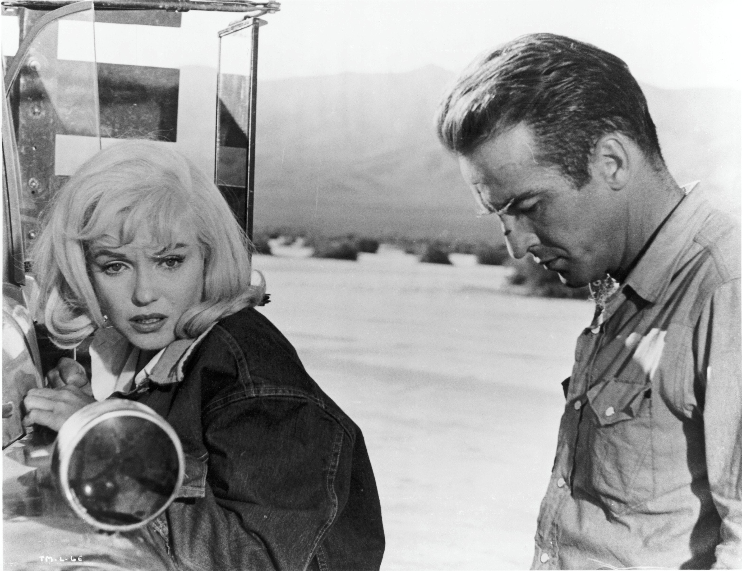 A morose man and woman next to a truck in a desert.