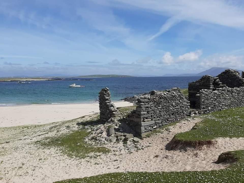 The ruins of a small stone cottage on a beach looking out to sea