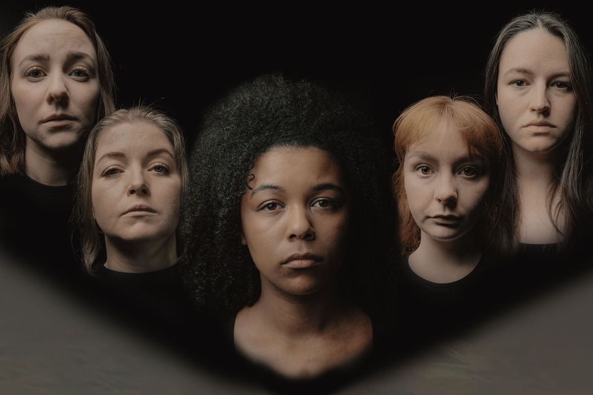 Head and shoulders of 5 serious looking women slightly blurred against dark background.