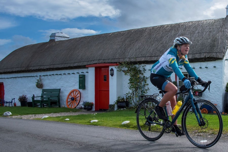 A cyclist passing a traditional thatched cottage