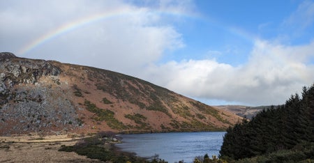 A view of a small mountain overlooking water with a rainbow over head
