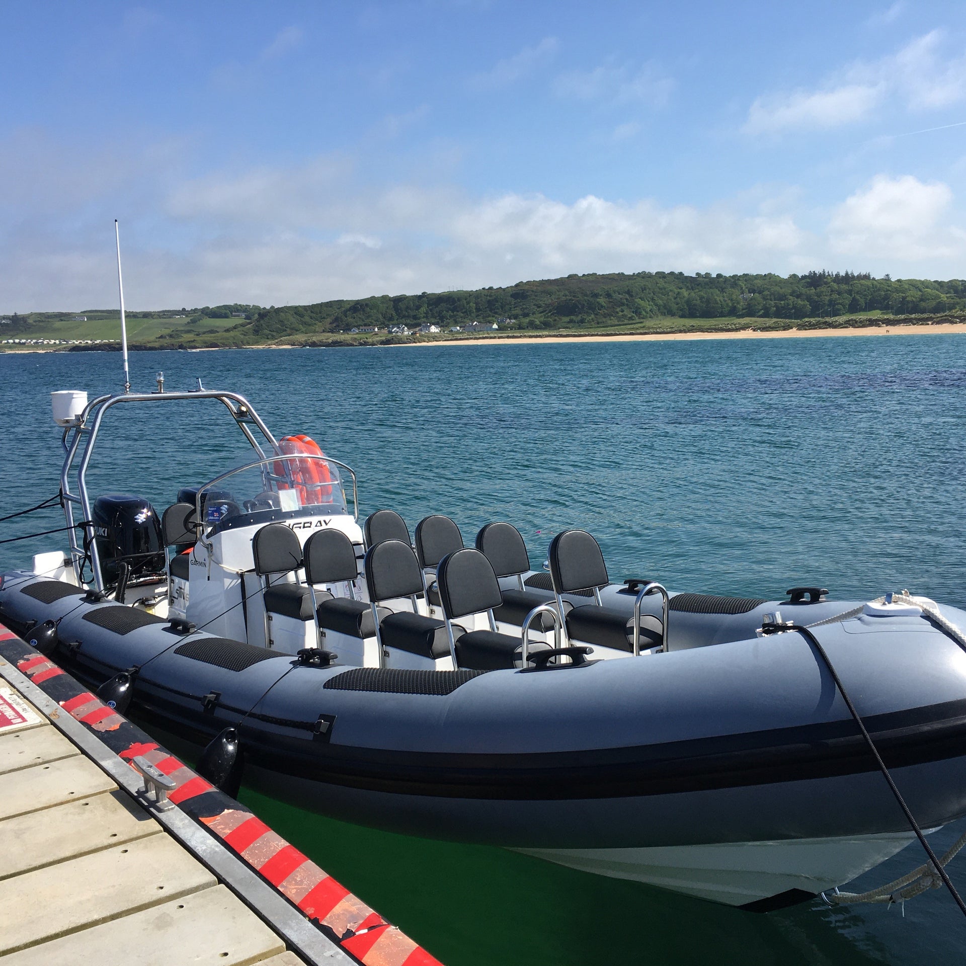 Eight seater rib on water moored at wooden pier with a beach and fields in the background
