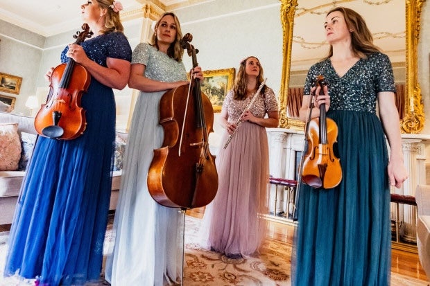 Glas Quartet, 4 women in long evening dresses holding musical instruments in an ornate room.