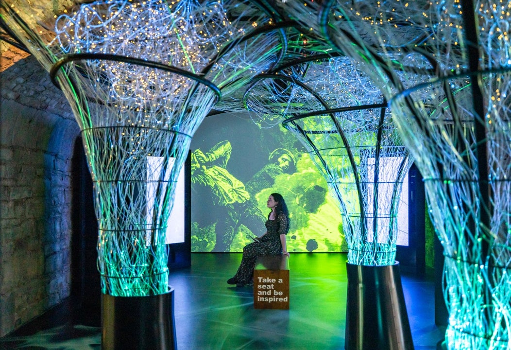 Person sitting in the middle of a room surrounded by green and blue lights