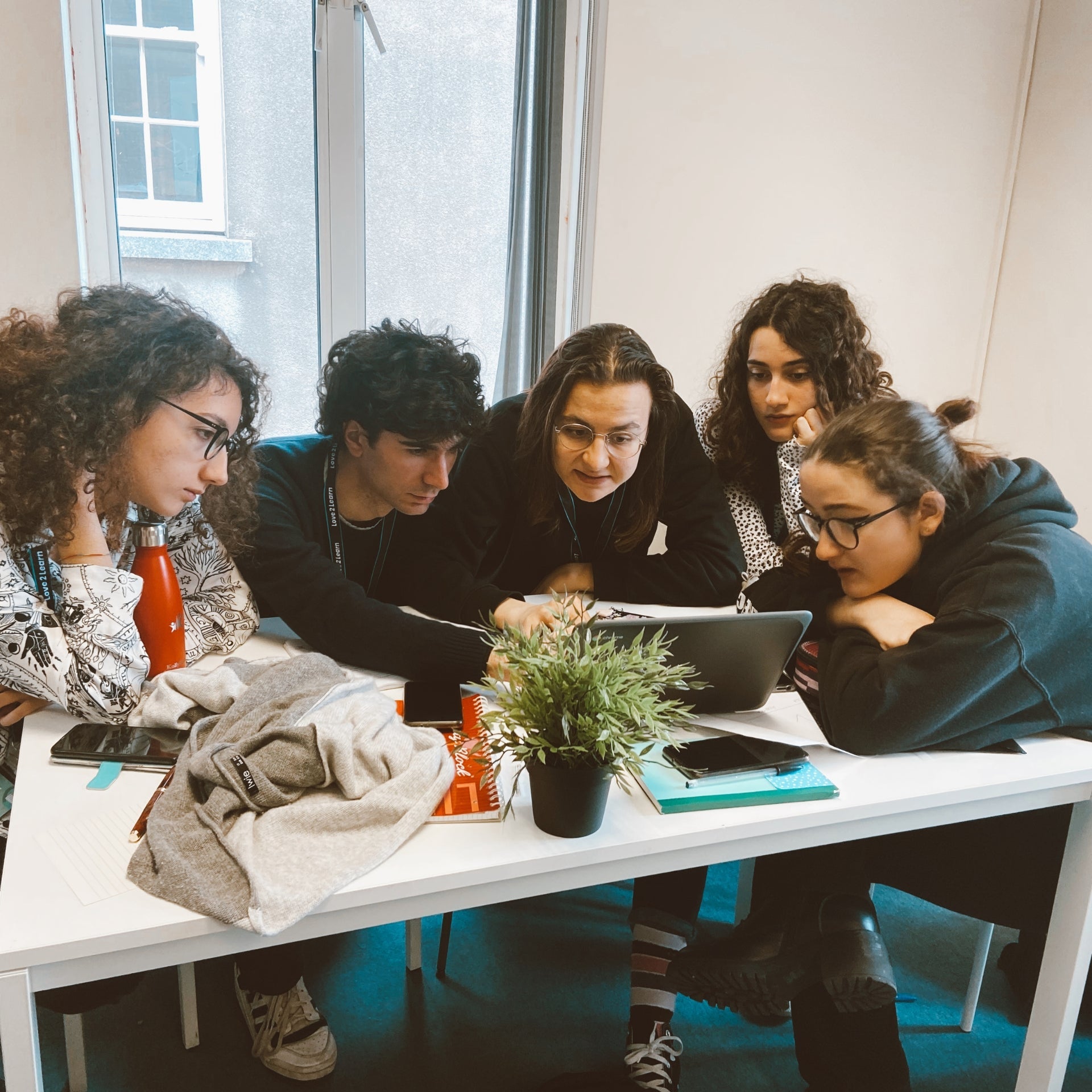 A small group of student and their tutor gather around to look at a laptop screen