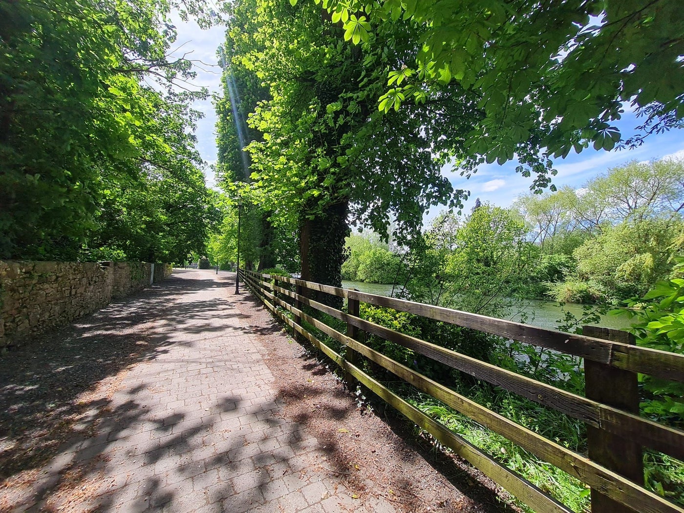 A path running along a river bank lined with a wooden fence