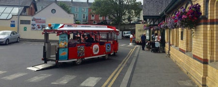 A small train on the road outside a train station
