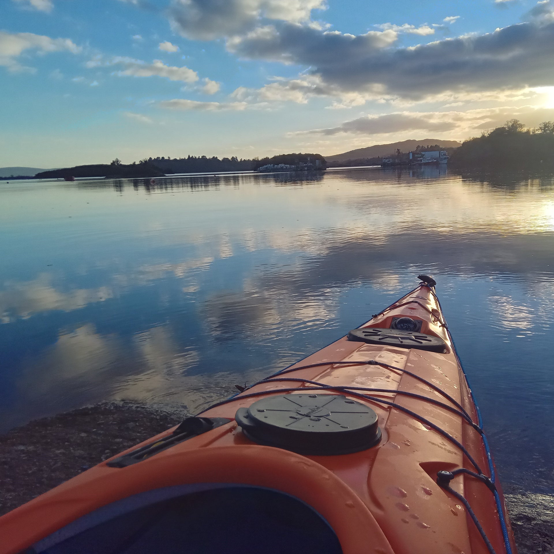 View from the front of an orange kayak overlooking the sea and bay at sunrise