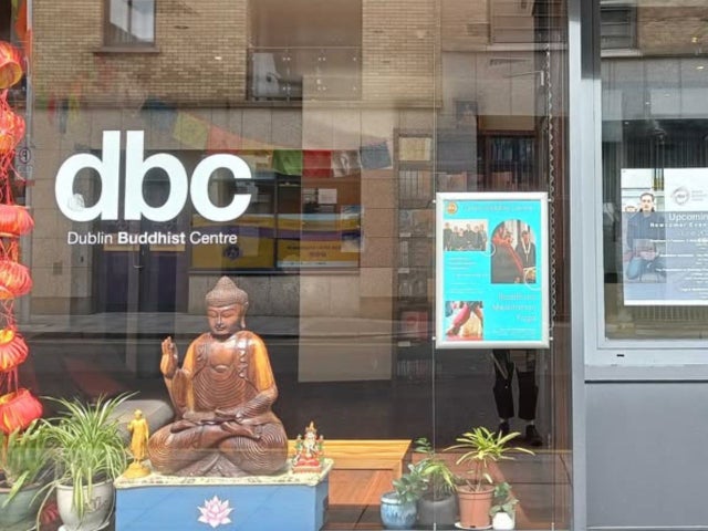 A window of a Buddhist centre with a Buddha in the window and a business logo