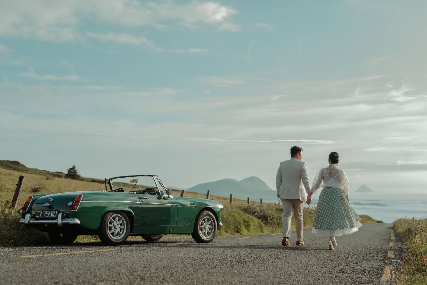 A couple walking hand in hand while passing a parked vintage car