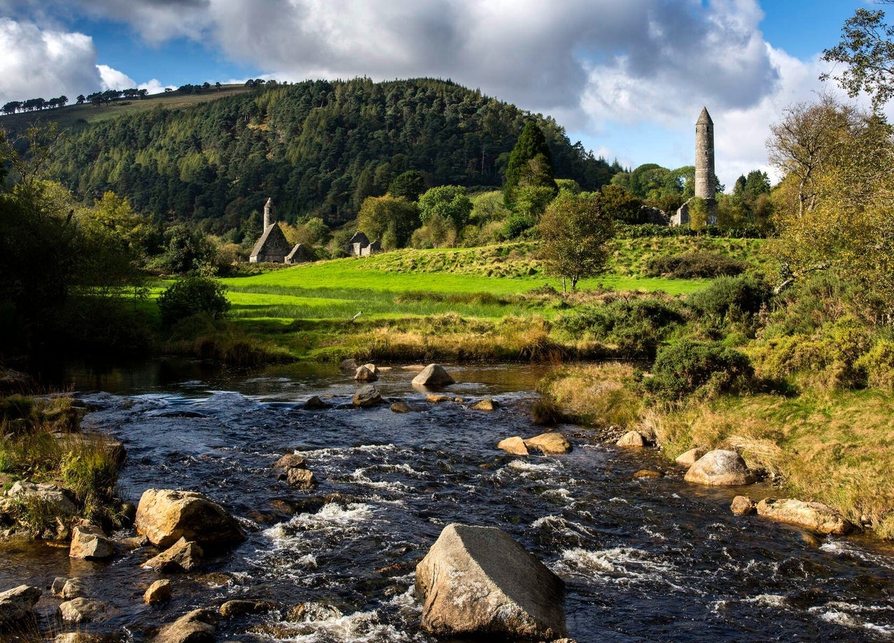 A river in front of Glendalough round tower and ancient monastic ruins