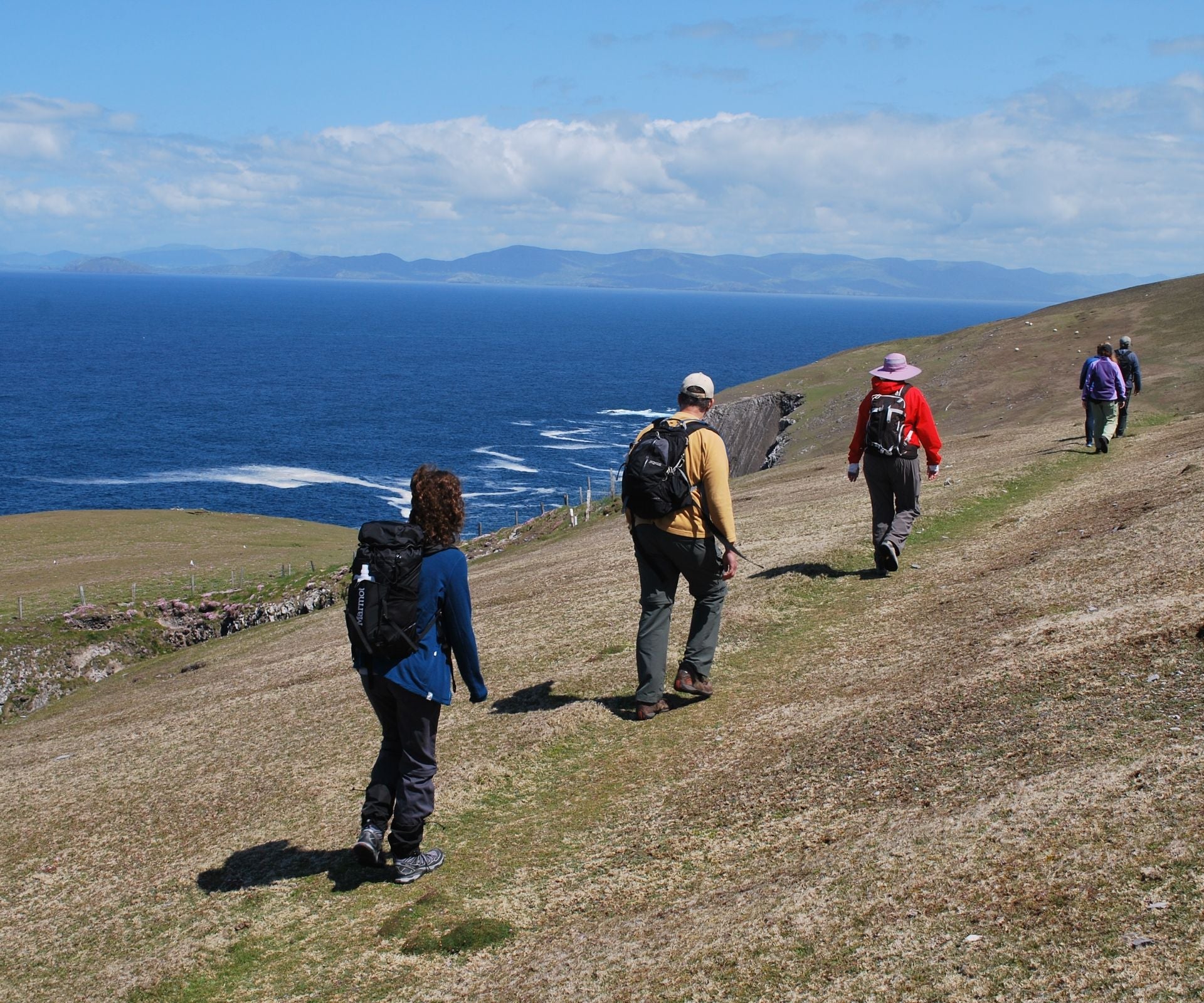 A walking group on a cliff walking with the ocean and mountains in the background