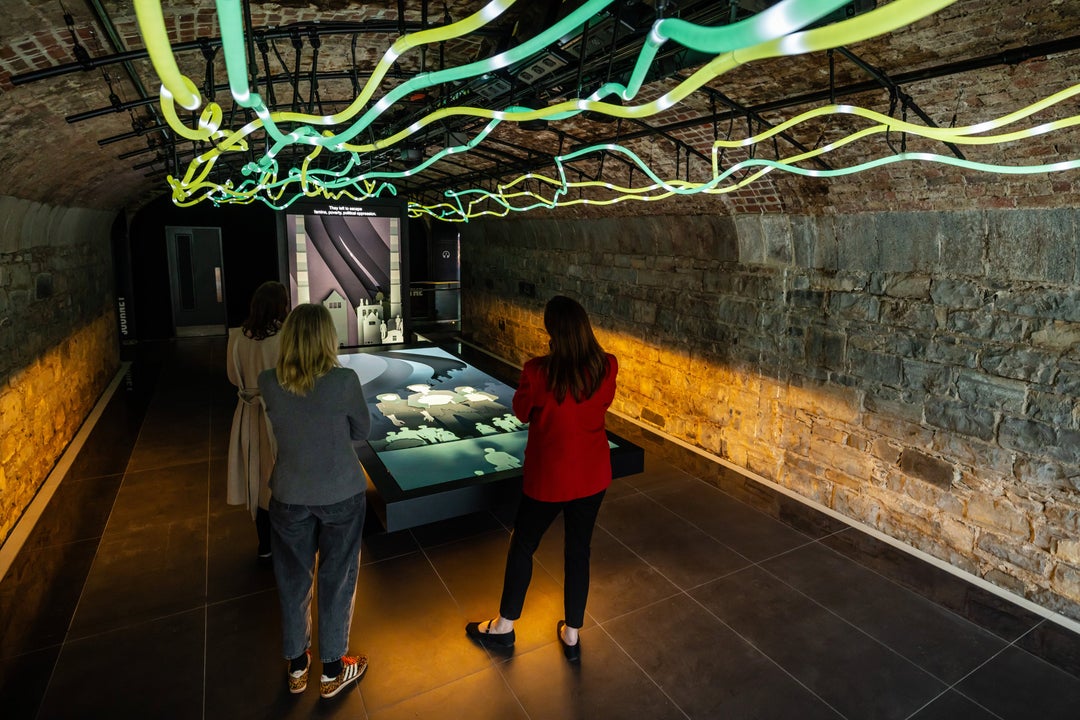 Three women looking at a large screen with coloured lights above their heads