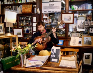 A musician holding a guitar inside Sweny's Pharmacy in Dublin City