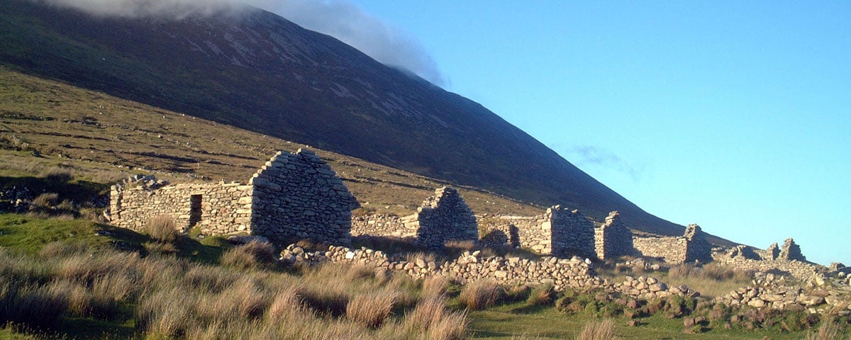 The ruins of stone cottages at the foot of a mountain with mist rolling down from the top of the mountain