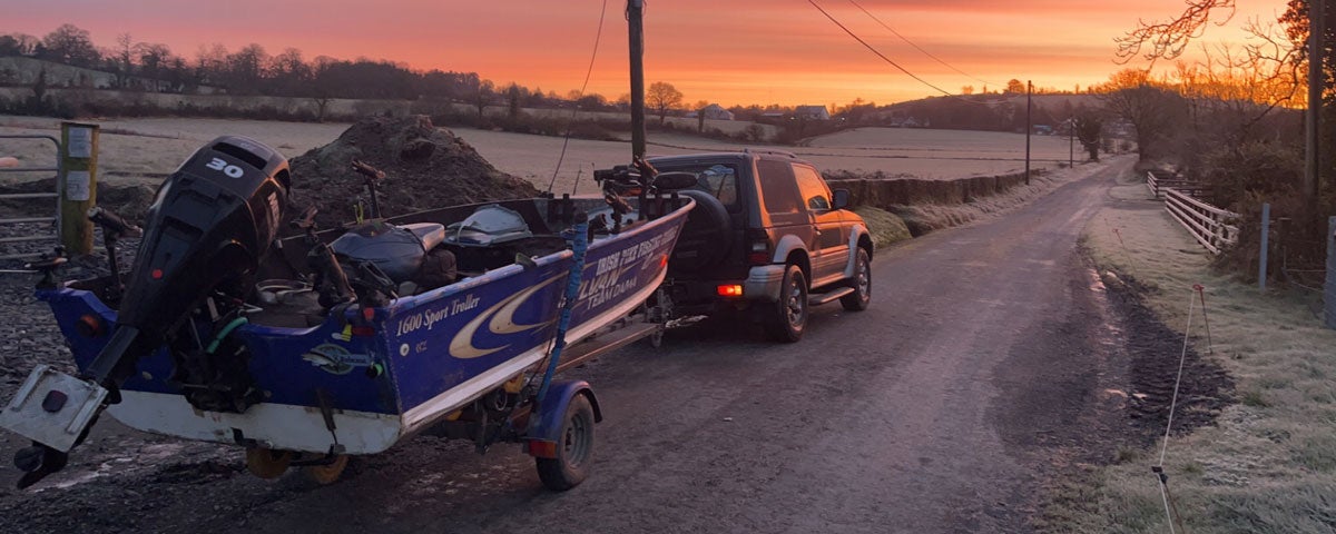 A jeep along the side of a road with a boat on a trailer at a colourful sunset